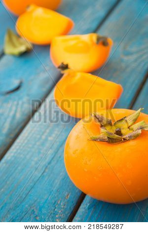 Delicious ripe persimmons in a raw on blue rustic wooden background close-up
