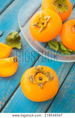 A glass plate of sweet orange persimmons on blue rustic wooden background closeup