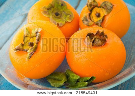 A glass plate of delicious ripe persimmons on blue rustic wooden background closeup