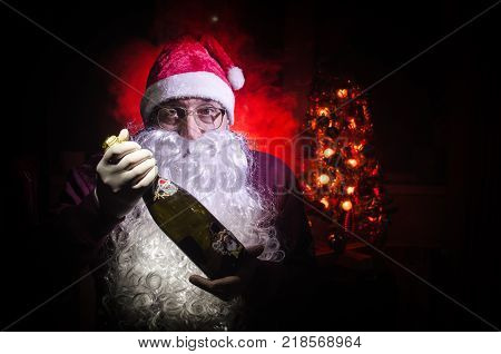 Santa Claus toasting with a glass of champagne (Bottle) Santa Claus with a glass of champagne celebrating and smiling. Selective focus dark toned background