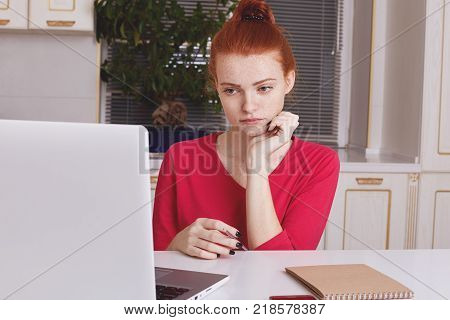 Attractive Female Student With Ginger Hair Bun Thinks About Coursework Strategy, Works With Laptop C