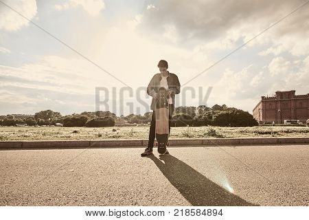 People youth urban lifestyle extreme sports and activity concept. Outdoor action shot of stylish young male in sneakers performing tricks using long board casting shadow of pavement. Warm filter