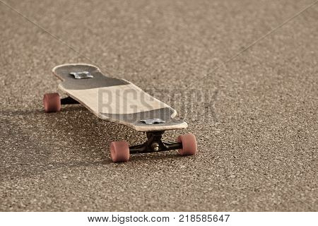 Outdoor picture of shabby skateboard with orange wheels resting isolated on textured paved concrete road left by its careless teen owner. Skateboarding youth subculture and urban lifestyle