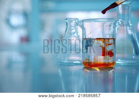 clear glass beaker with orange drop solution in chemistry science laboratory background
