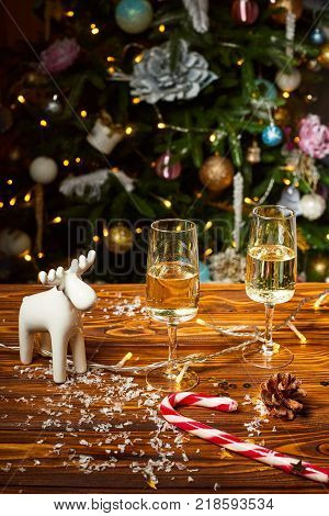 New year and Christmas decoration on the wood table . Christmas deer on the wooden table with wineglasses and lights on the background