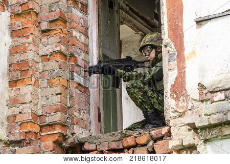 Portrait of armed woman with camouflage. Young female soldier observe with firearm. Child soldier with gun in war hearth house ruins background. Military army people concept