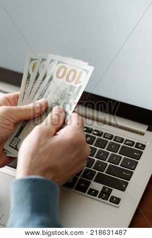 Online casino gambling. Man holding money and placing virtual bets using laptop. Luck success and winning concept