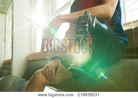 Close up of amputee sportsman sitting on bench in modern gym, focus on prosthetic leg in sunlight with lens flare