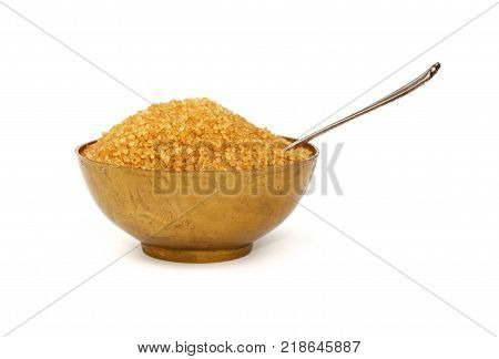 Close up one vintage bronze metal bowl full of raw brown cane sugar with antique spoon isolated on white background low angle side view