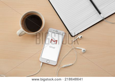 KIEV, UKRAINE - OCTOBER 12, 2017: Modern iPhone SE Rose Gold with Gmail app on screen, cup of coffee and earphones on wooden table