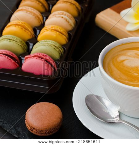 French makarons on a black background and a cup of your favorite coffee to sweets.