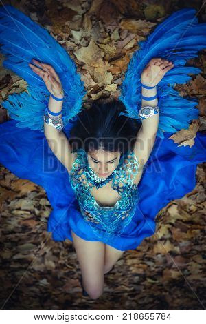 Fairy, Gothic beautiful brunette girl in a suit made of blue wires, bears bird wings and colorful feathers helmet