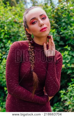 Beautiful young woman with long braid wearing tight dress and natural cherry earrings in summer park.