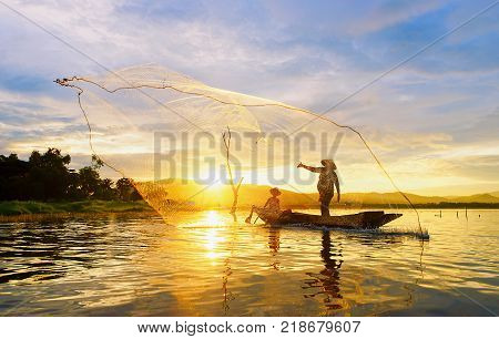 Fisherman on wooden boat casting a net for catching freshwater fish in reservoir