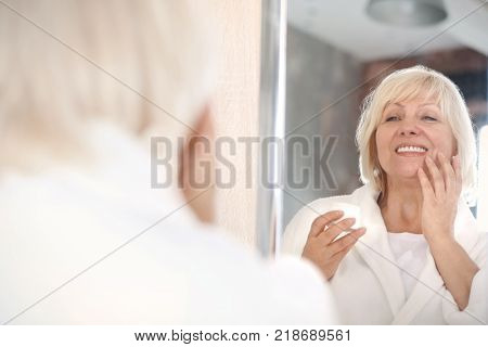 Mature woman applying anti-aging cream at home