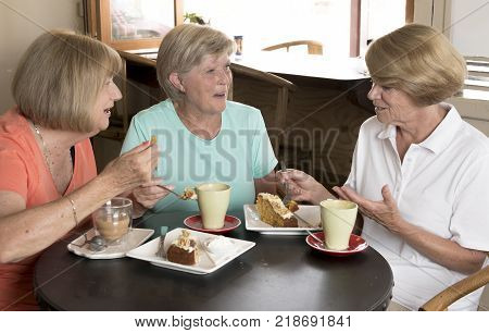 group of three lovely middle age senior mature women girlfriends meeting for coffee and tea with cakes at coffee shop sharing time together enjoying converstion happy and cheerful gossiping