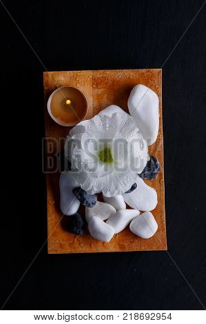 A bud of a white beautiful flower, a small burning candle and a multiform pebble, for spa treatments on a small wooden board. Close-up. View from above.