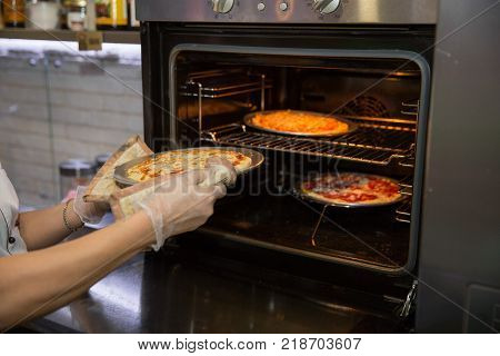 Cropped shot of hands of the cook in kitchen glove taking pizza from oven. readiness test
