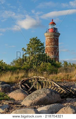 Lighthouse and old boat in the Baltic Sea. Shore, evening light, sunset, clouds and architecture concept. Mohni, small island in Estonia, Europe.