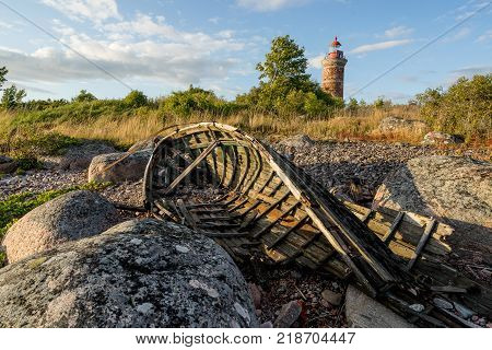 Lighthouse and old boat in the Baltic Sea. Shore, evening light, sunset, clouds and architecture concept. Mohni, small island in Estonia, Europe.