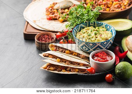 Homemade beef meat mexican fajitas with tortilla and guacamole and salsa sauces over black background