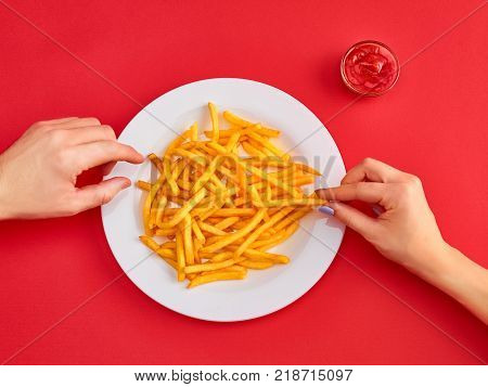 Young woman and man eating french fries potato with ketchup in a restaurant, having her lunch break. Close up