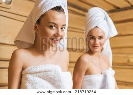 attractive young women covered with towels relxing in sauna and looking at camera