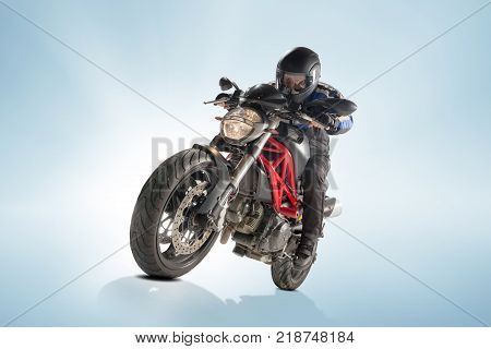 Biker in black jacket and helmet sitting on his sportive bike on blue studio background
