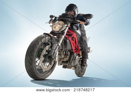 Biker in black jacket and helmet sitting on his sportive bike on blue studio background