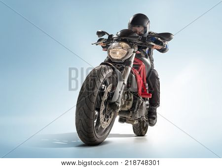 Biker in black jacket and helmet sitting on his sportive bike on blue studio background