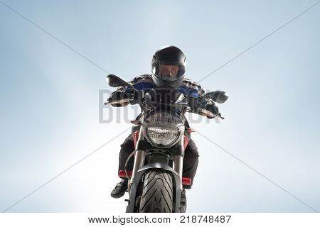 Biker in black jacket and helmet sitting on his sportive bike on blue studio background