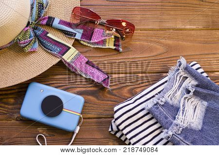 Woman paking for a travel. A straw hat, a camera, sunglasses and summer clothes on a rustic wooden background, top view.
