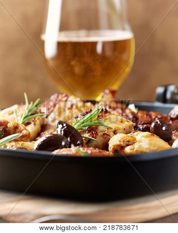 Grilled chicken pieces with olives in a pan and glass of beer