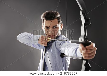 Young businessman practicing archery on dark background