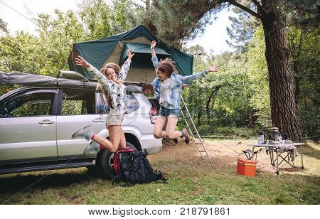 Young beautiful women friends jumping in a campsite into the forest. Leisure time and enjoyment concept.