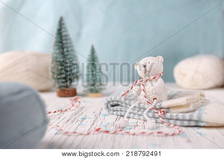 White yarn with two christmas trees and souvenir white teddy bear which sits on the striped socks.