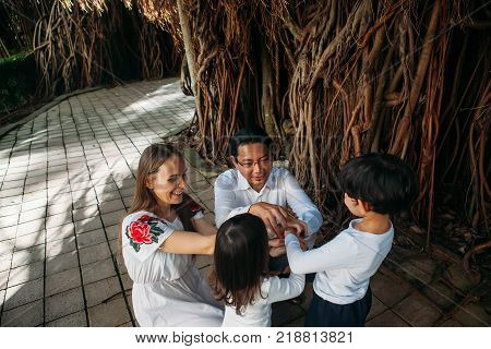 happy stylish multinational parents holding hands with son and daughter walking in jungles park, amazing family moment. father's mother's day