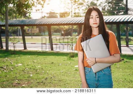 A young or teen asian girl student in university and holding the laptop computer in summer holiday in the park.