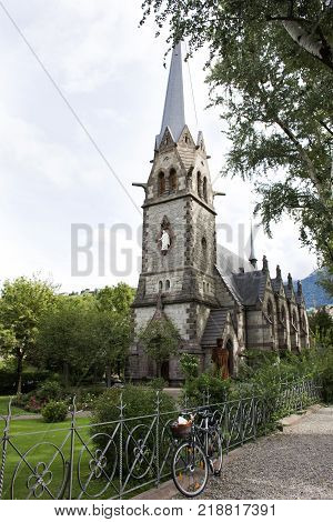 Travelers people stop bicycle and visit relax at garden of Chiesa evangelica di Cristo church at walkway riverside passer river in Meran city in Merano Italy