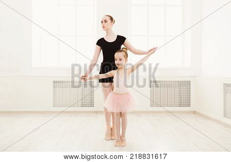 Little girl learning ballet with teacher copy space. Cute small ballerina training classical dance exercises with female coach.