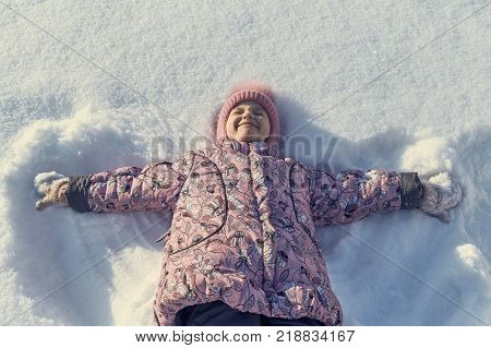 Girl lying on her back in the snow hand in hand. The girl narrowed her eyes and wrinkled my nose and smiles. She was pleased and happy. Tracks in the snow from his hands like the wings of an angel.