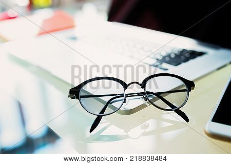Close up of eye glasses on work desk with laptop at workplace.