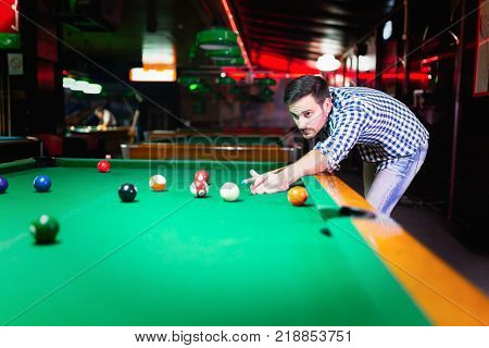 Hansome man playing pool in bar alone aiming