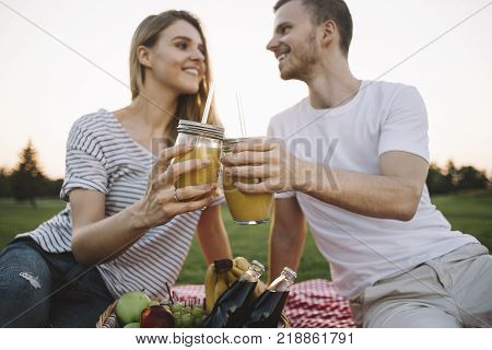 One more close up of beautiful and cheerful couple drinking some orange juice outside in park and looking to each other. They have big plans together for the future where they will be happy. Cut view