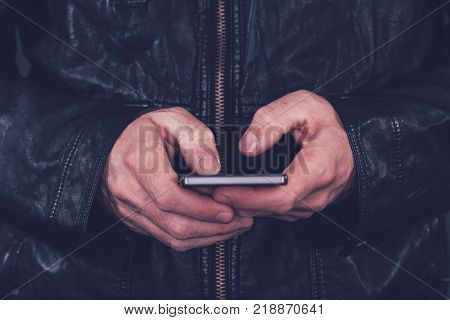 Man in leather jacket using mobile phone for texting. Modern technology and lifestyle concept.