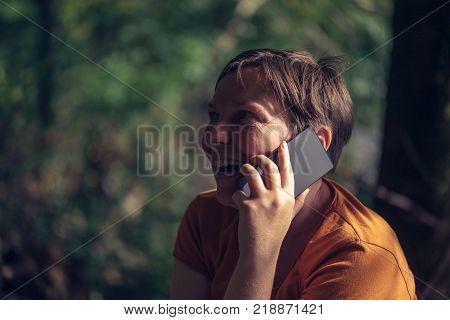 Happy smiling woman talking on mobile phone outdoors in park on sunny summer afternoon
