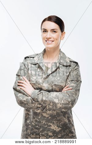 Country in safe. Merry enthusiastic confident woman woman  wearing  combat uniform and crossing her hands while   standing  on the  isolated  background