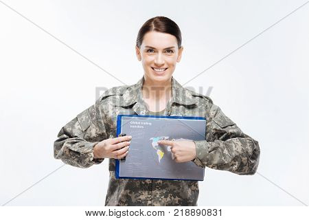 Region searching. Cheerful young tranquil woman  smiling to the camera   and wearing combat  uniform while pointing at map