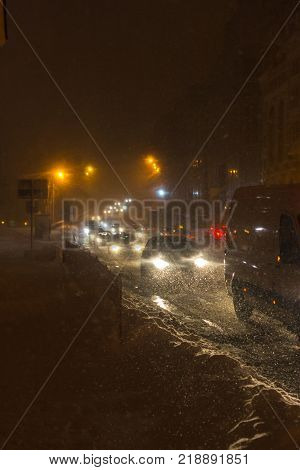 A car driving on the road in the aggravated traffic due to strong snowfall. City blizzard. City light, night.