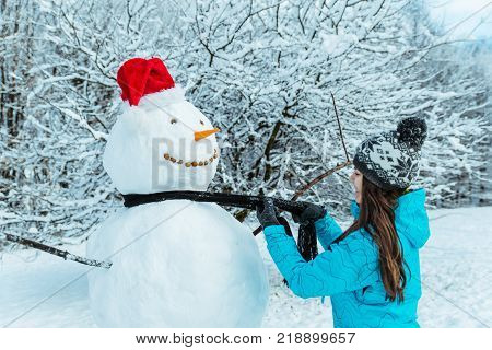 woman making snowman in winter day put carrot as nose